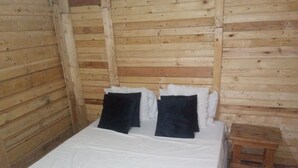 Una habitación tipo cabaña de madera con una cama, almohadas y un taburete de madera.