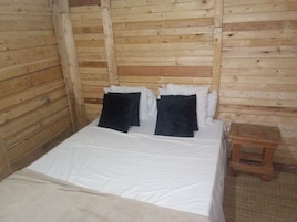 Una habitación tipo cabaña de madera con una cama, almohadas y un taburete de madera.