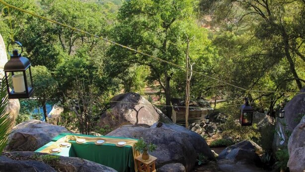 Un comedor con una mesa lista para cuatro personas, rodeado de rocas grandes y follaje.