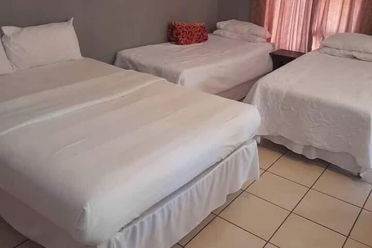 Una habitación de hotel con tres camas, una mesita pequeña y una cortina.