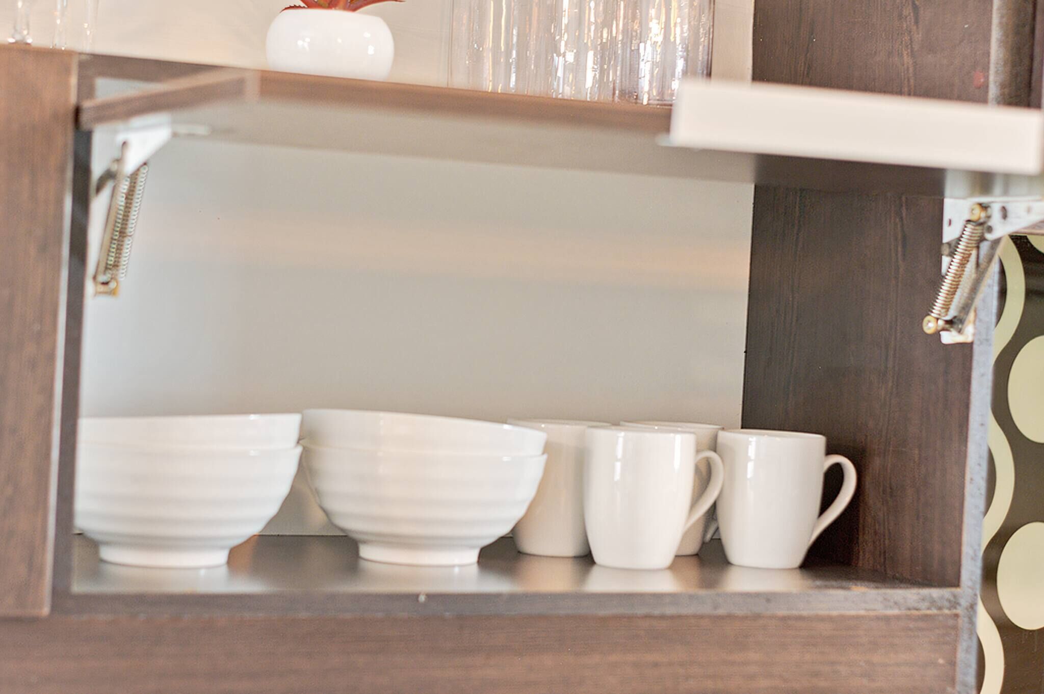 A kitchen cabinet with white bowls and mugs.