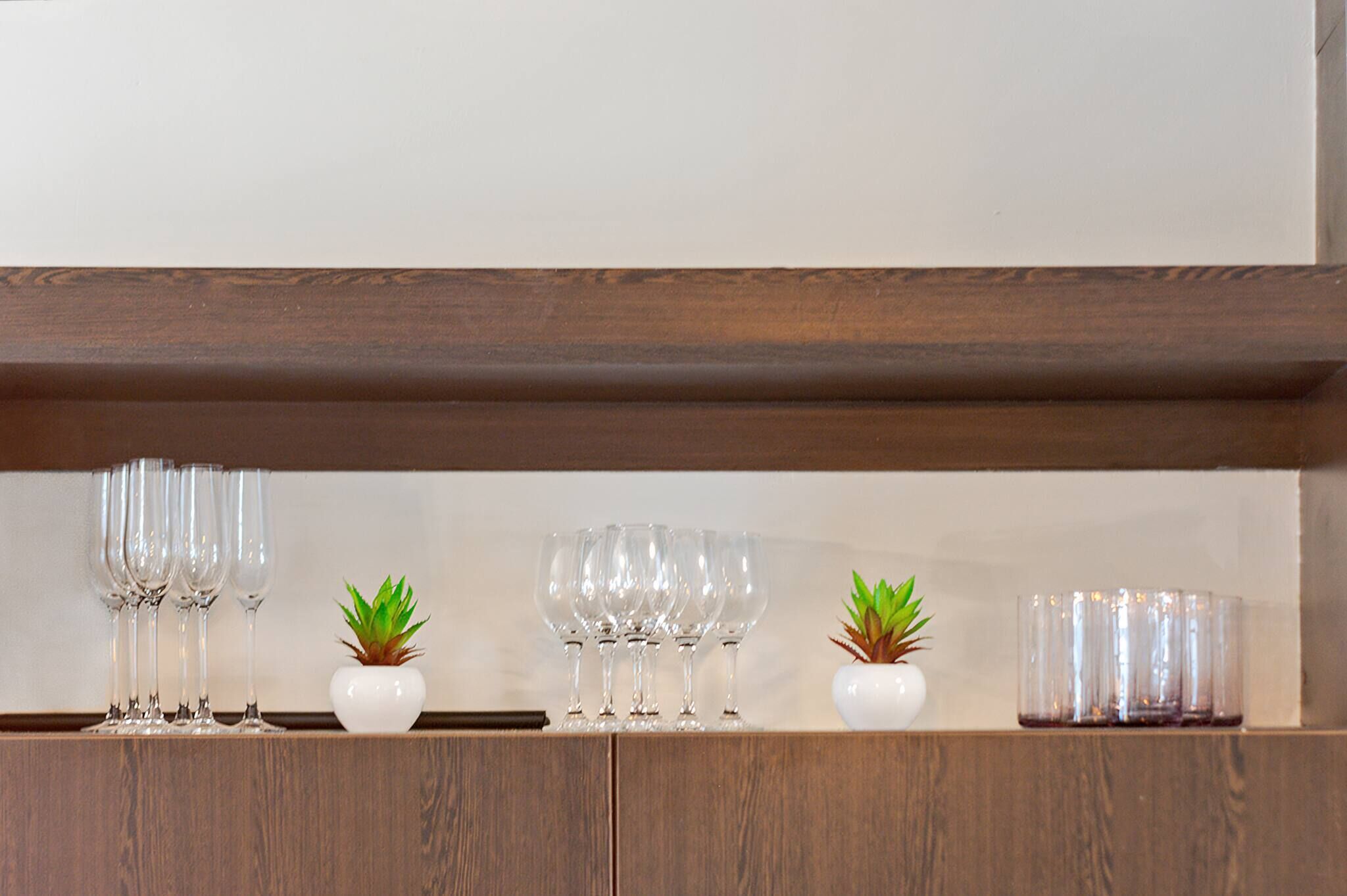 A wooden shelf with clear glassware and small potted plants.