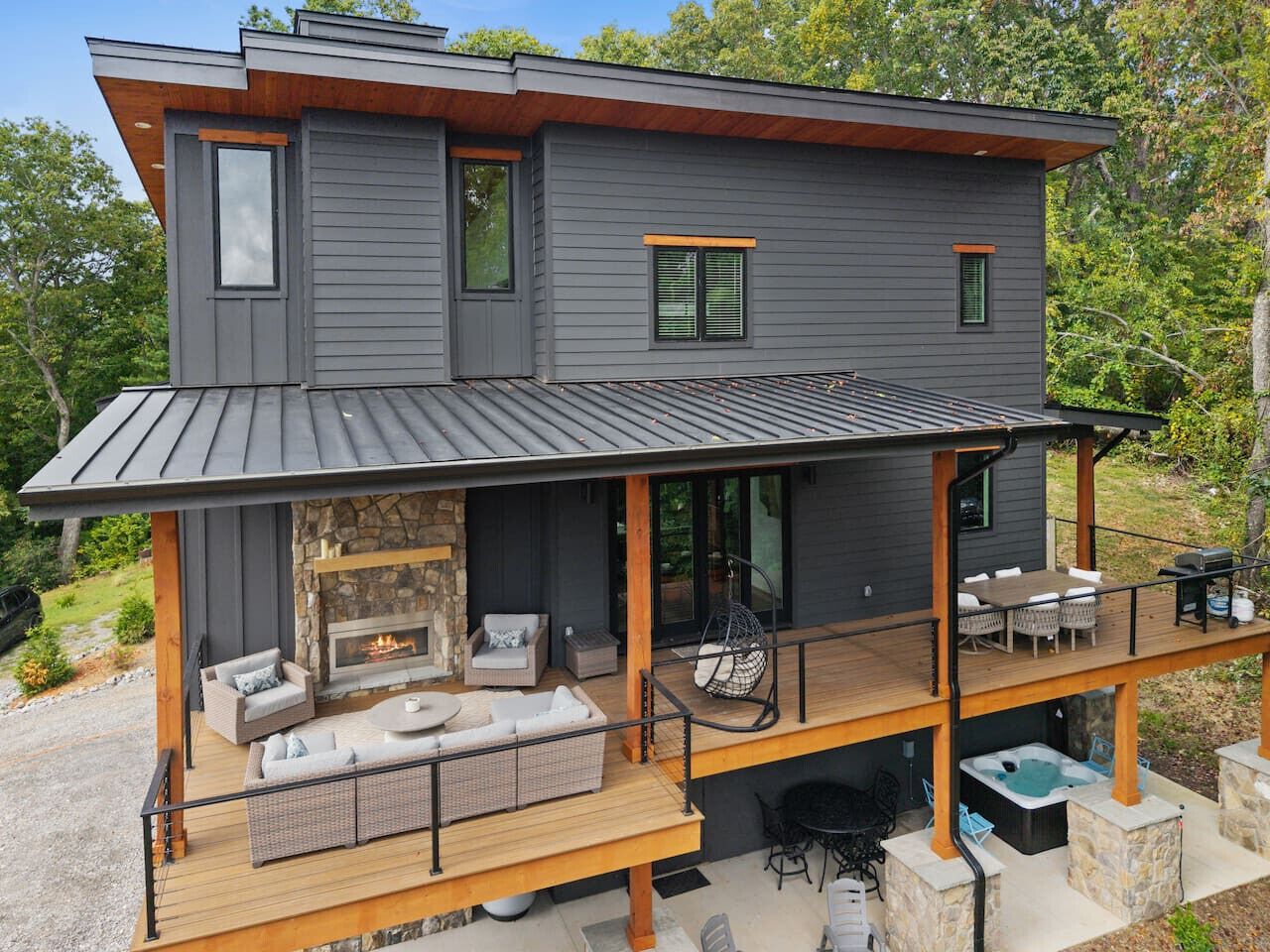 Une maison moderne à deux étages dotée d’une terrasse couverte, d’un espace salon extérieur et d’une cheminée.