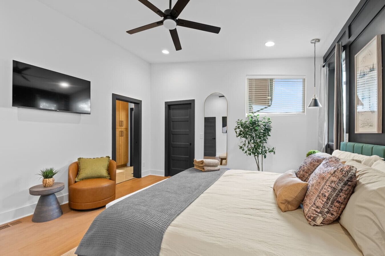 Une chambre à coucher avec un lit, un ventilateur de plafond, une télévision, une plante et une fenêtre.