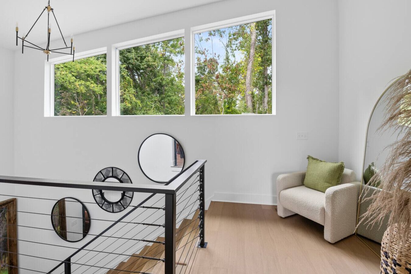 Un intérieur moderne avec un escalier, un canapé blanc agrémenté d’un coussin vert et un grand miroir.