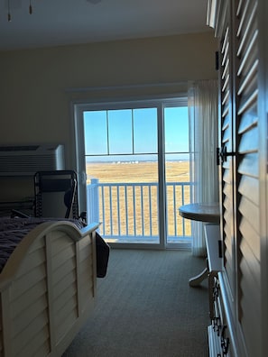 A hotel room with a bed, a chair, a small table, a radiator, and a view of the beach through a sliding glass door. -   Seabrook Sweet Beach condo beautiful water view 5 minute walk to the beach (Seabrook)