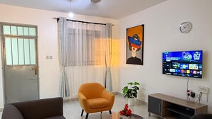 A living room with a sofa, armchair, coffee table, TV, ceiling fan, and a door with a window. - Edinah Homes in Shanzu,Mombasa,Kenya,the beach 5 minute (Mombasa)