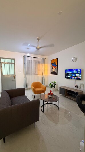 Ein Wohnzimmer mit Sofa, Sessel, Couchtisch, Fernseher, Deckenventilator und einer Tür mit Fenster.