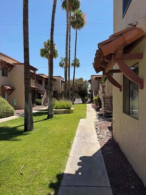 A pathway flanked by palm trees leading to a building with a red awning and a visible staircase. - Quiet Tucson Hideout +pool +patio (Tucson)