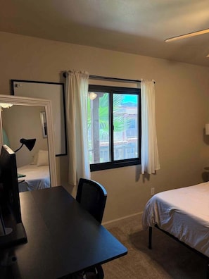 A room with a bed, a desk, a chair, a window with curtains, and a view of buildings outside. - Quiet Tucson Hideout +pool +patio (Tucson)