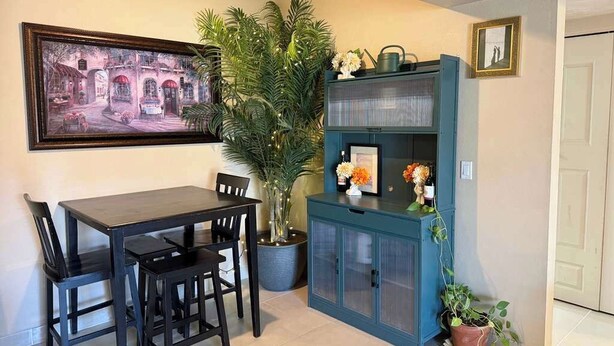 Un comedor con una mesa y sillas, una planta en maceta, un armario con puertas de cristal y un cuadro en la pared.