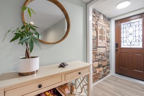 Ein Flur mit Blumentopf, rundem Spiegel, Steinwand und Holztür.
