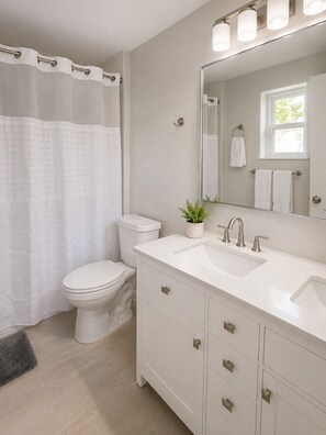 Une salle de bain avec un rideau de douche, des toilettes, un lavabo, un miroir et une petite plante en pot.
