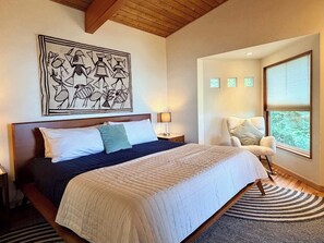 A bedroom with a large bed, a wooden ceiling, a wall art piece, a chair, and a window with blinds.