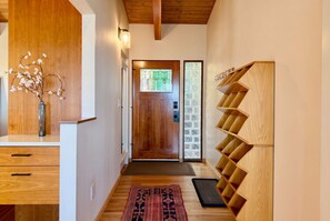 A hallway with a wooden door, a wall-mounted shelf, and a rug on the floor.