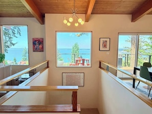A staircase with wooden railings, a ceiling light fixture, and a large window with a view of the sea.