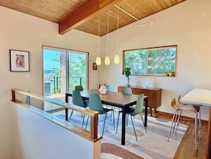 A modern dining area with a wooden ceiling, large windows, and a view of greenery.