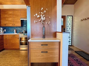 A modern kitchen with wooden cabinets, a built-in oven, and a decorative vase with flowers.