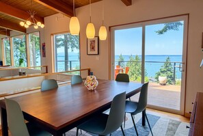 A dining area with a wooden table, chairs, pendant lights, and a view of the sea through large windows.