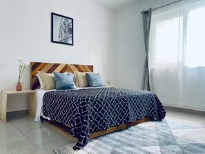 Ein Schlafzimmer mit Bett, Nachttisch, gerahmtem Bild an der Wand und einem Fenster mit Vorhängen.