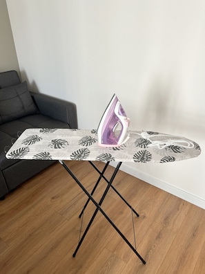 A table with an ironing board and an iron, a grey sofa, and a wooden floor. - Cozy studio Beige - close to city centre (Warszawa)