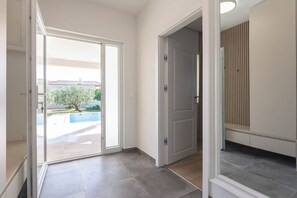 Ein Flur mit einer Schiebetür, die zu einem Poolbereich führt, einer geschlossenen Tür und einer Wand mit vertikalen Jalousien.