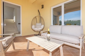 Ein Balkon mit einer Couch, einem Hängesessel, einem Tisch und einer Weinflasche.
