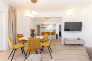 Ein modernes Wohnzimmer mit Essbereich, einer Küche im Hintergrund und einem an der Wand befestigten Flachbildfernseher.