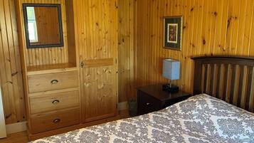 Een slaapkamer met houten lambrisering, een bed met beddengoed met een patroon, een dressoir, een spiegel, een ingelijst schilderij en een nachtkastje.
