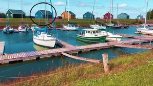Un puerto deportivo con barcos amarrados, muelles de madera y varias casas pequeñas al fondo.