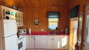 Cocina con paneles de madera, armarios blancos, refrigerador, microondas y pileta.