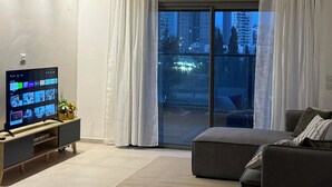 Moderni olohuone, jossa on taulutelevisio, sohva ja suuri liukuovi, joka johtaa parvekkeelle.