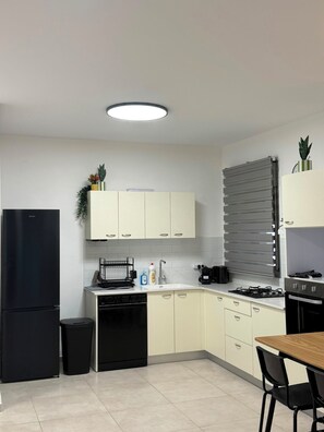 Ett modernt kök med ett svart kylskåp, vita skåp, ett matbord i trä och en svart spis.