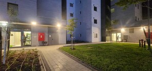 En modern byggnad med en stenlagd innergård, en liten gräsmatta och en röd elcentral.
