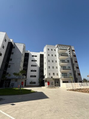 A modern multi-story building with a flat roof, large windows, and a central entrance. - K-Home 3 Bedroom Karme Gat - Kiriat Gat (קריית גת)