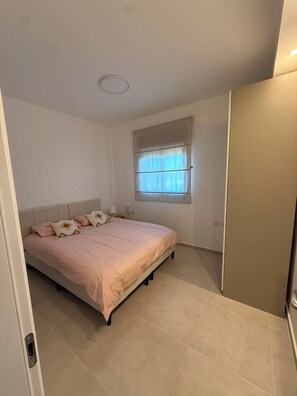 Et soveværelse med seng, gardiner ved et vindue, en dør og en lampe i loftet.