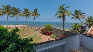A coastal view with palm trees, a beach, and a garden with pink flowers. - Dutch Point Beach Resort - Negombo (Negombo)