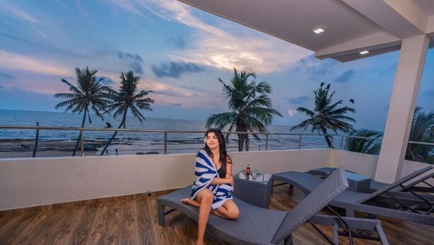 A person sitting on a lounge chair on a balcony with a view of the ocean and palm trees. - Dutch Point Beach Resort - Negombo (Negombo)