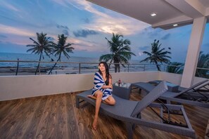 A person sitting on a lounge chair on a balcony with a view of the ocean and palm trees. - Dutch Point Beach Resort - Negombo (Negombo)