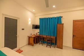 Une pièce comprenant un lit, un bureau avec des chaises, une télévision et une porte.