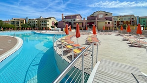 Una piscina con lettini e ombrelloni, circondata da edifici colorati.