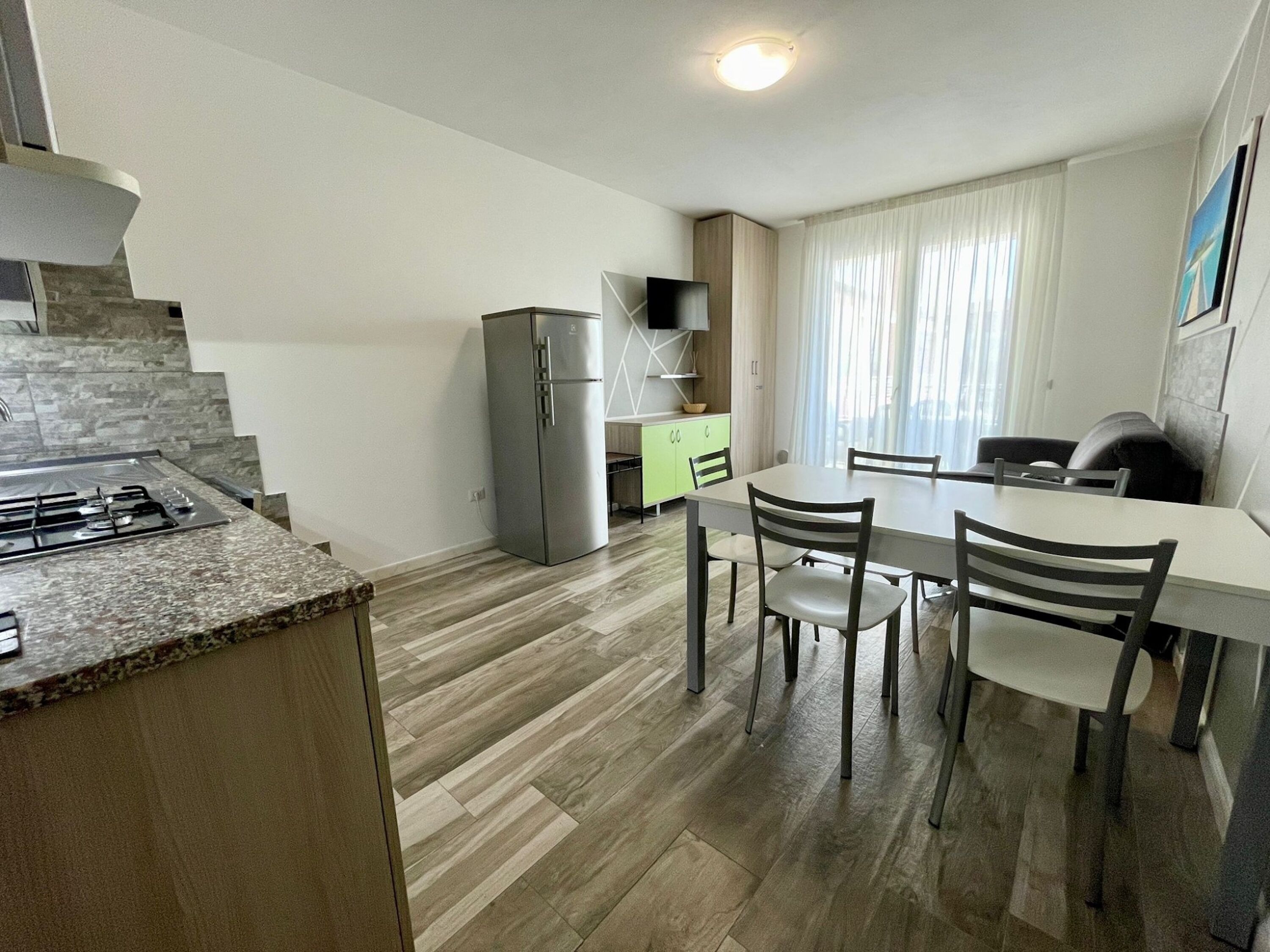 A modern kitchen with a gas stove, a built-in oven, and a refrigerator. There is a dining area with a table and chairs.