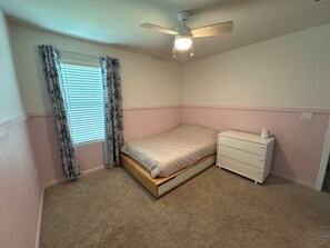 Une chambre à coucher avec un lit, une commode, un ventilateur de plafond et une fenêtre avec des rideaux.