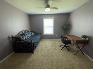 Une chambre à coucher avec un lit, un bureau, une chaise, un ventilateur de plafond et une fenêtre.