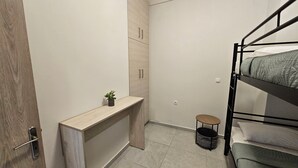 Een kleine kamer met een stapelbed, een klein bureau, een stoel en een pot met een plant.