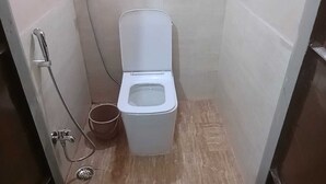 A small, enclosed bathroom with a white toilet, a showerhead, and a bucket. - 2kms  to hawamahal homestay in jaipur (Jaipur)