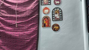 A room with a pink patterned fabric draped over a chair, a white wall with decorative wooden cutouts, and two colorful stools with intricate designs. - 2kms  to hawamahal homestay in jaipur (Jaipur)