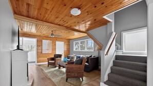 A spacious room with a wooden ceiling, a staircase, and a view of the outdoors.