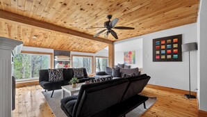 A spacious living room with a wooden ceiling, large windows, and a modern sofa set.