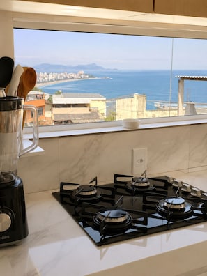 A kitchen with a gas stove, a blender, and a window with a view of the sea and buildings. - Ap Favela Chic, very cozy. With a hot tub and barbecue, 700 meters from the beach. (Rio de Janeiro)